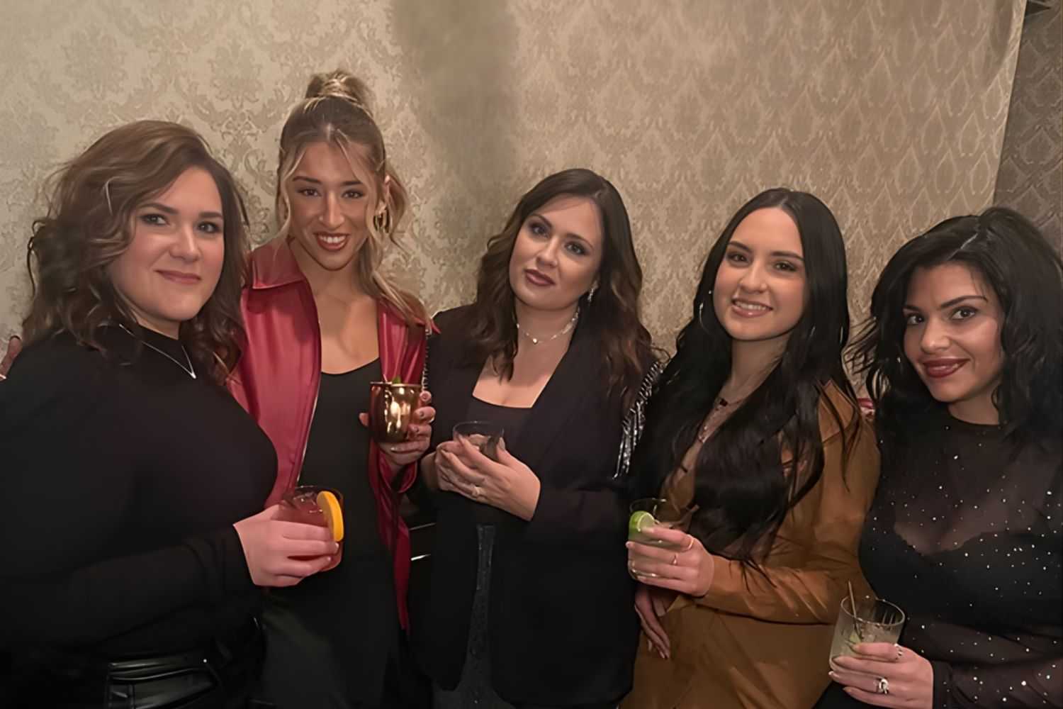 Group of five women enjoying drinks at a social gathering indoors.
