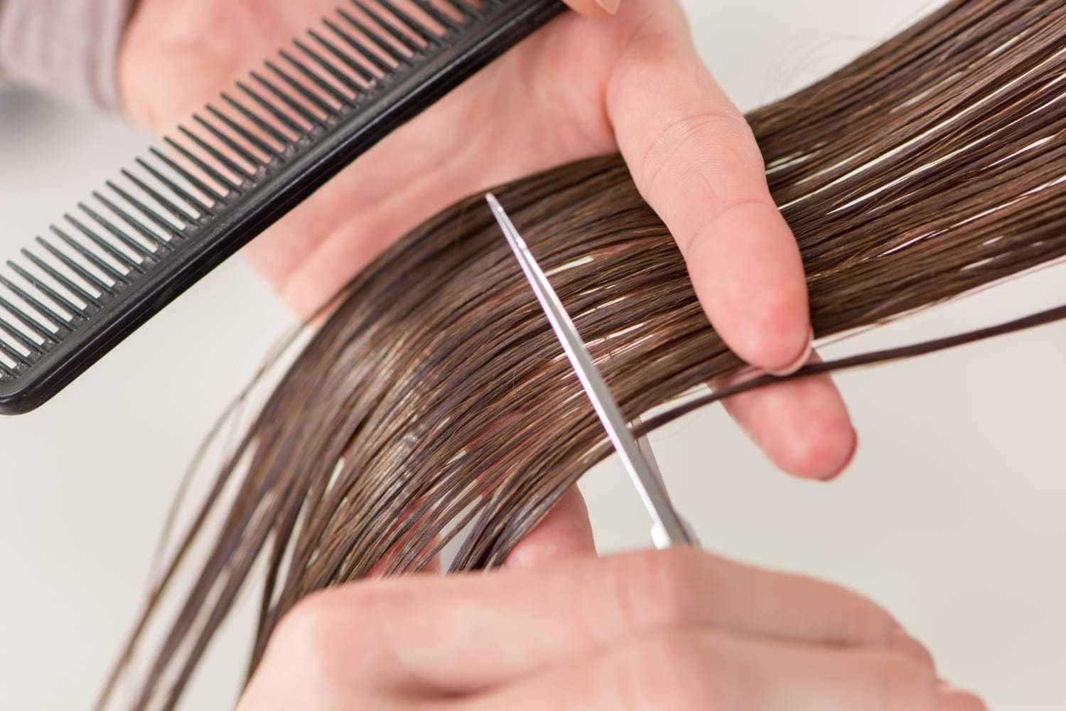Hands cutting brown hair with scissors and comb.